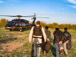 A man assisting three individuals hands tied boarding a helicopter
